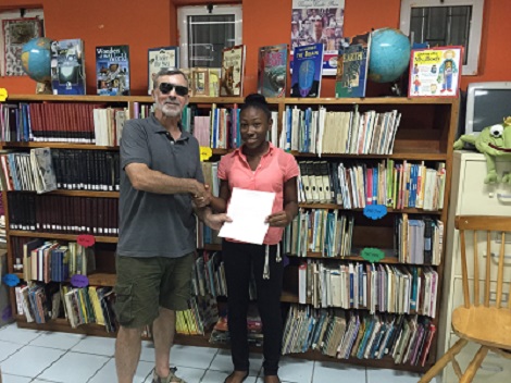 Photo of AtO scholar receiving her award, shaking hands with sponsor, books in background.